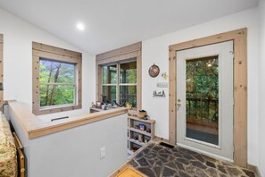 Una habitación con suelo de piedra, vigas de madera, estante empotrado y puerta que da a una terraza.