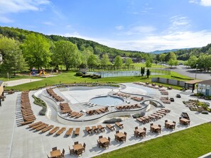 Piscina con sillones y mesas, rodeada de jardines con árboles y vistas a un paisaje montañoso.