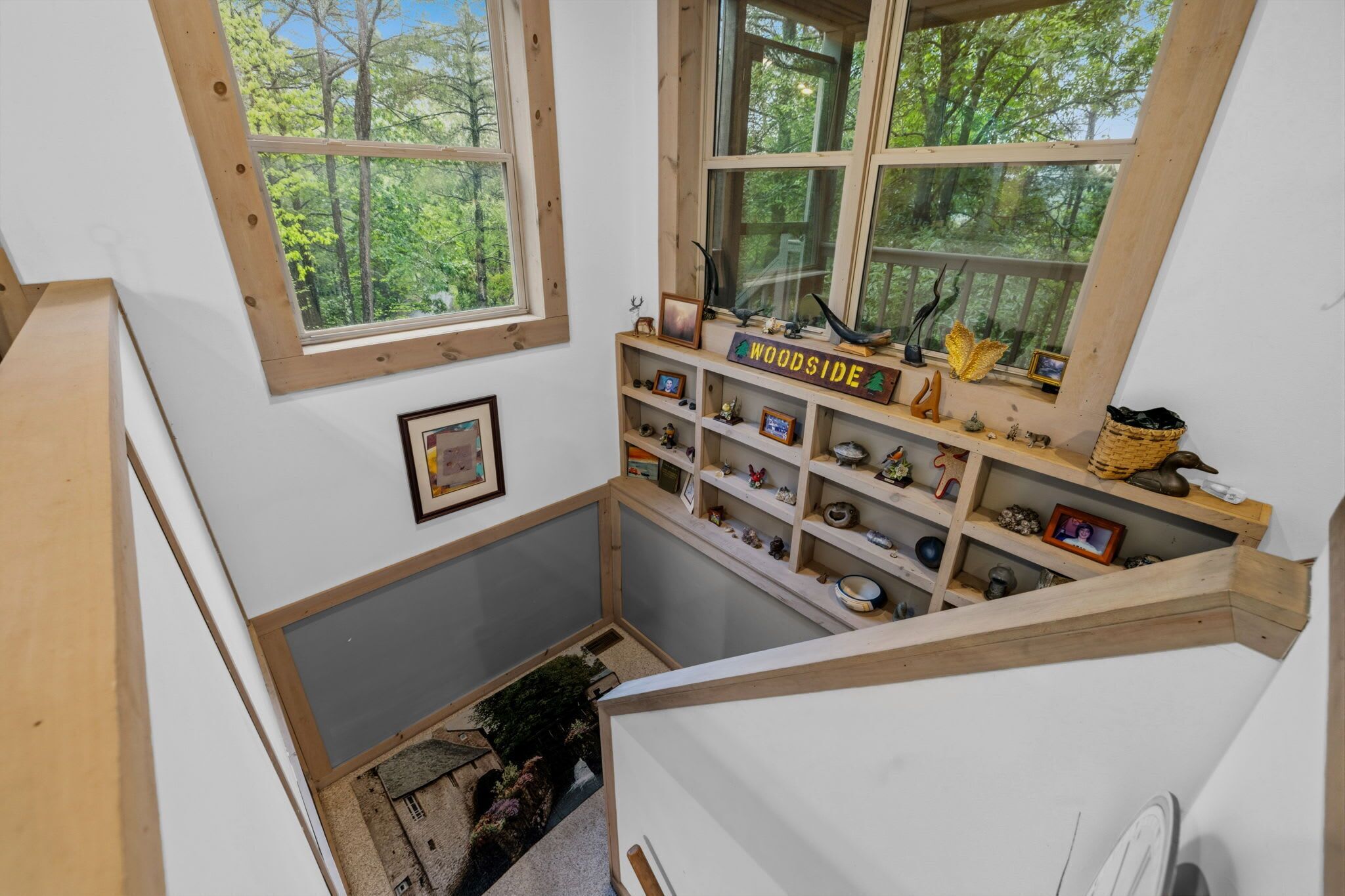 Una habitación con techo inclinado, estantes de madera con diversos objetos, un letrero que dice 'WOODSIDE' y una ventana con vista a un bosque.