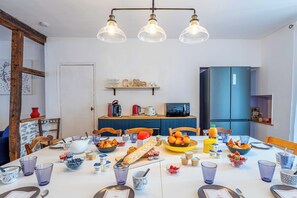 A dining table set with various food items, a coffee station, and a kitchen area with appliances. - L'Escapade Minervoise, the ideal place to stay with family or friends (Laure-Minervois)