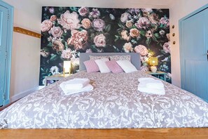 A bedroom with a floral wallpaper, a bed with a patterned bedspread, two bedside tables with lamps, and a wooden headboard. - L'Escapade Minervoise, perfect for families or friends   (Laure-Minervois)