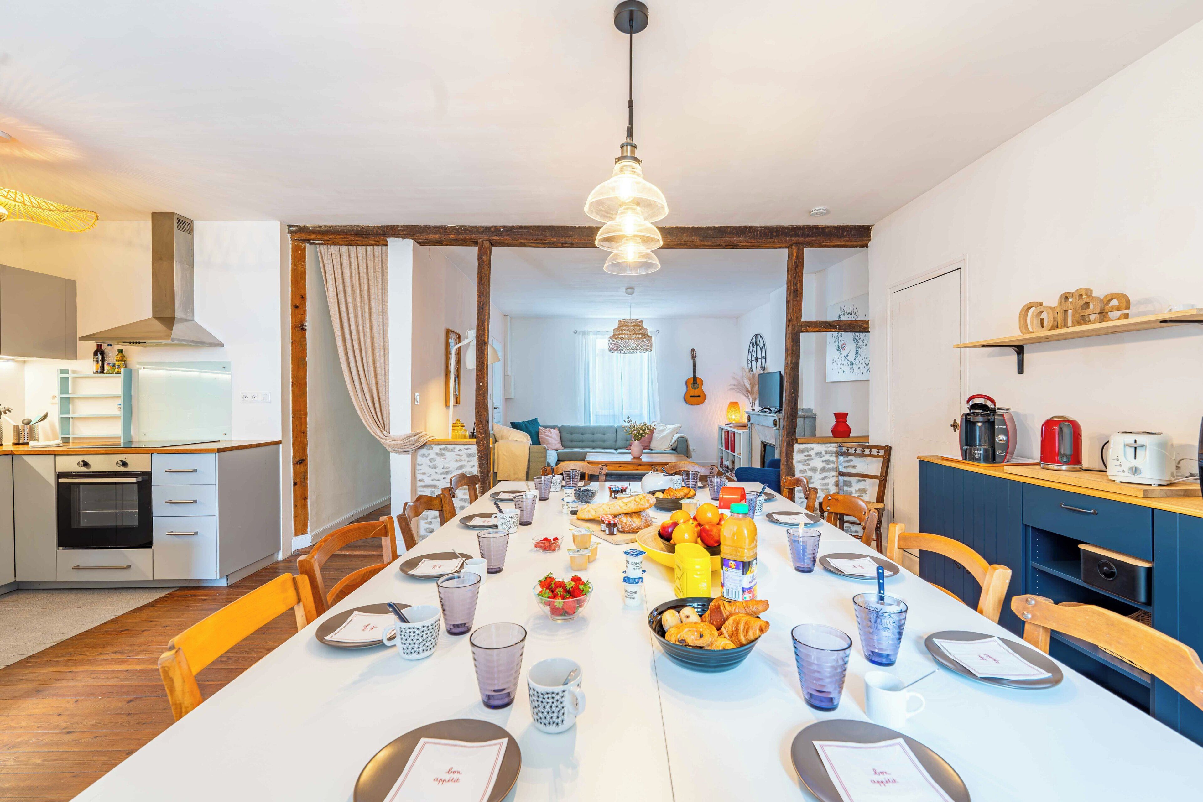 Een eetgedeelte met een lange tafel gedekt voor een maaltijd, keukenapparatuur en een koffiehoek.
