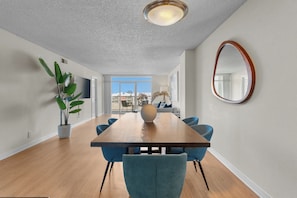A modern dining room with a wooden table, blue chairs, a large mirror, and a potted plant.