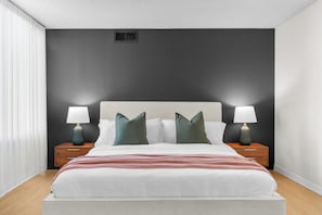 A modern bedroom with a large bed, two bedside tables with lamps, and a dark accent wall.