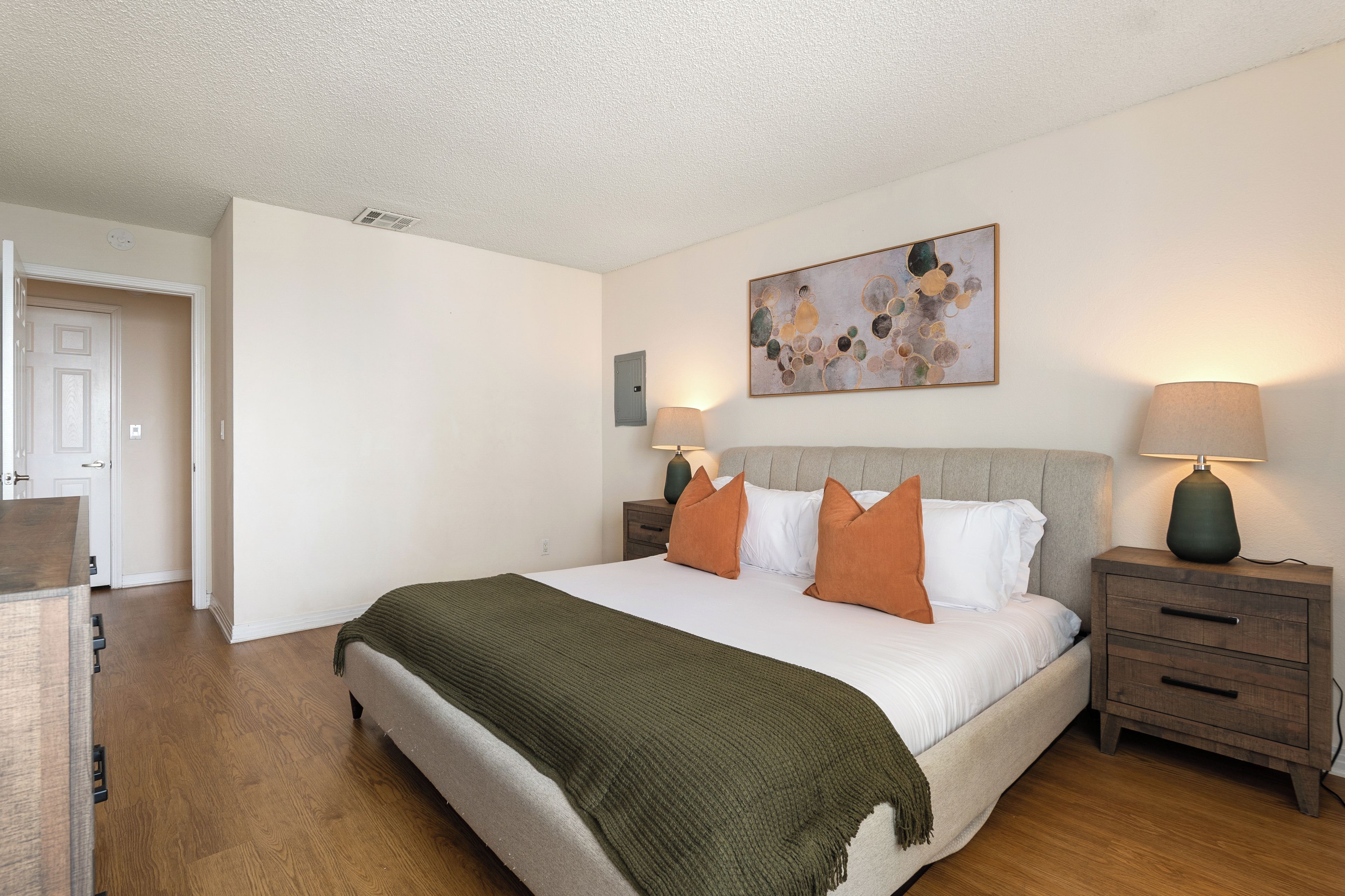 Une chambre à coucher comprenant un lit, deux tables de chevet, une commode, une porte et une œuvre d’art accrochée au mur.