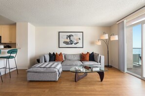 A modern living room with a grey sectional sofa, a glass coffee table, and a painting on the wall. - Sunset Pearl' Full Ocean Views Pool Gym & Parking Available (Marina del Rey)