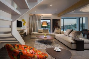 Ein modernes Wohnzimmer mit einer Couch, einem Couchtisch und einem farbenfrohen Sessel. Eine Treppe mit einem besonderen Design führt auf eine weitere Ebene.