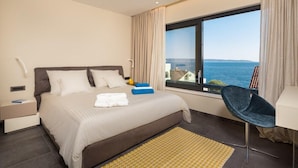 Een moderne hotelkamer met een groot bed, een bureau, een stoel en uitzicht op de zee.
