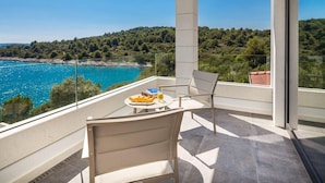 Een balkon met een tafel, stoelen en uitzicht op zee en bos.