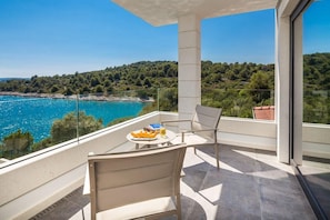 Ein Balkon mit Tisch, Stühlen und Blick auf das Meer und den Wald.
