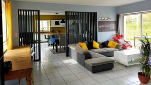 Una sala de estar moderna con un sofá modular, un comedor y una cocina al fondo.