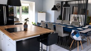 Una cocina moderna con una isla de madera, taburetes negros y un comedor con mantel azul y separador a rayas.