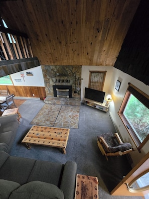 Una sala de estar acogedora con chimenea de piedra, un televisor de pantalla plana y un ventanal con vistas al exterior.