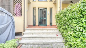 A building with a green door, steps leading to the entrance, and a covered area to the left. - Il Rifugio di Manu (Lucca)