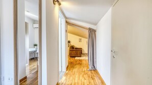 A hallway with wooden flooring, a mirror, a door, and a glimpse of a living area with a sofa and a plant. - Il Rifugio di Manu (Lucca)