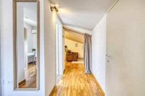 Un pasillo con suelo de madera, un espejo, una puerta y una vista parcial de una sala de estar con un sofá y una planta.