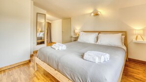 A neatly made bed with pillows and towels, a bedside table with a lamp, a mirror, and a wooden floor. - Il Rifugio di Manu (Lucca)