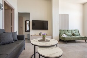 Ein modernes Wohnzimmer mit einem grauen Sofa, einem grünen Sofa, einem an der Wand montierten Fernseher und einem kleinen Tisch mit einem Blumenstrauß.