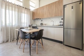Eine moderne Küche mit Esstisch, Stühlen, einem Kühlschrank und einem Fenster mit Vorhängen.