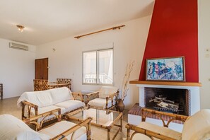 A living room with a fireplace, wicker furniture, a large window, and a red accent wall.