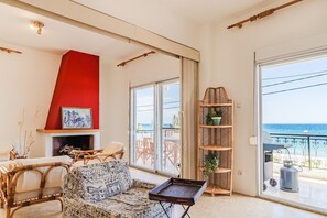 A living room with a fireplace, a sofa, a dining area, and a balcony with a view of the sea. - 10 Steps to the beach by Rentals Pro - Kalives Halkidiki (Kalyves Polygyrou)