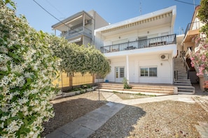 A two-story residential building with a balcony, a small garden area with gravel and stepping stones, and a fence.