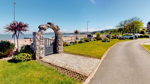 Una strada costiera con un arco in pietra, aree verdi e vista sul mare.