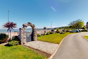 Eine Küstenstraße mit einem steinernen Torbogen, Grünflächen und Blick aufs Meer.
