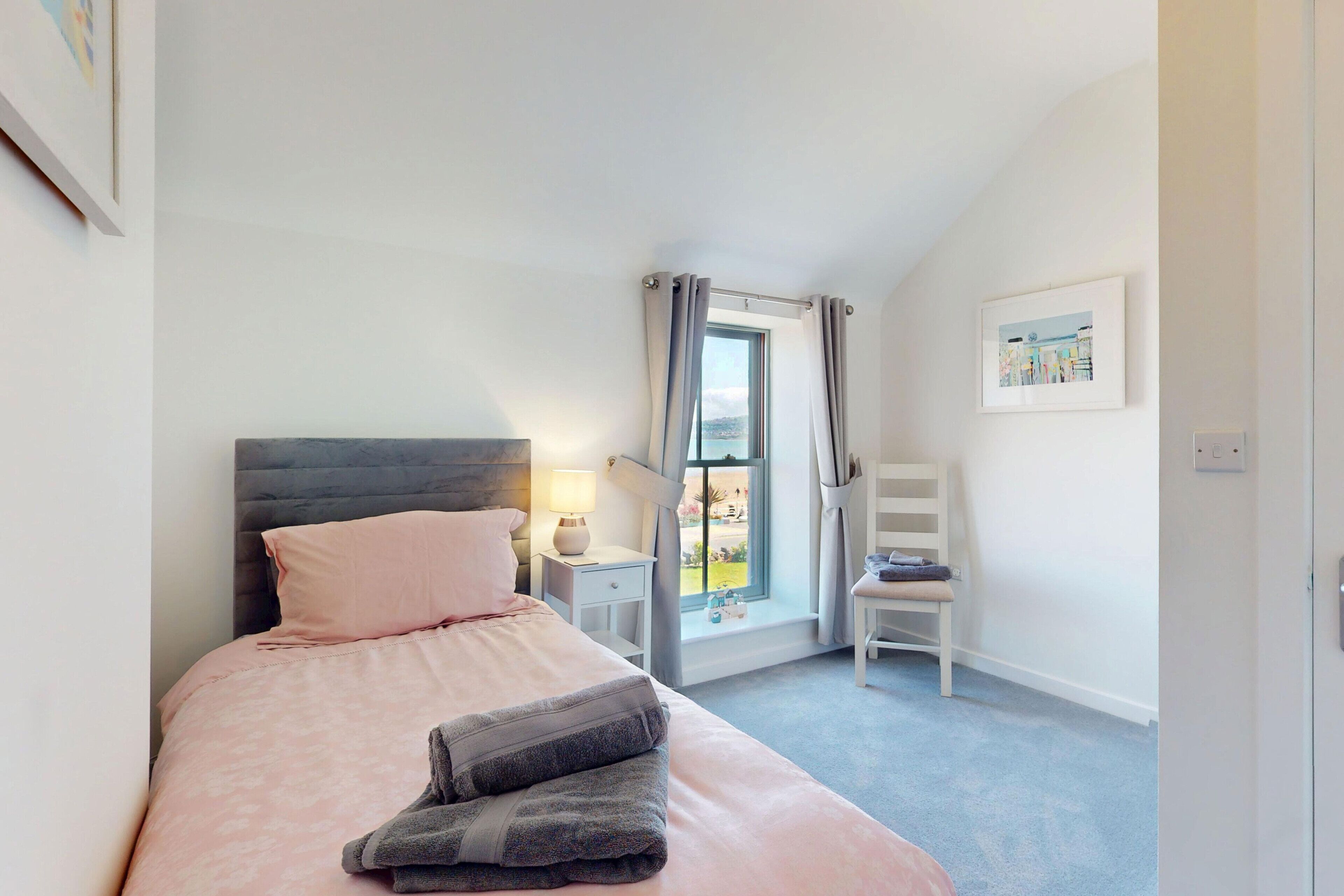 A bedroom with a bed, a nightstand, a chair, a window with curtains, and a framed picture on the wall.