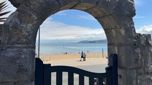 Un arco che conduce a una spiaggia, con vista libera sul mare e montagne in lontananza.