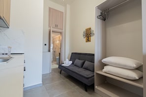 Eine moderne Wohnung mit Küche, einem grauen Sofa, einem Kleiderschrank mit Kleidung und einem Badezimmer im Hintergrund.