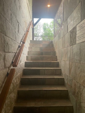 Eine Steintreppe mit Holzgeländern, die zu einem überdachten Bereich mit Blick auf Bäume führt.