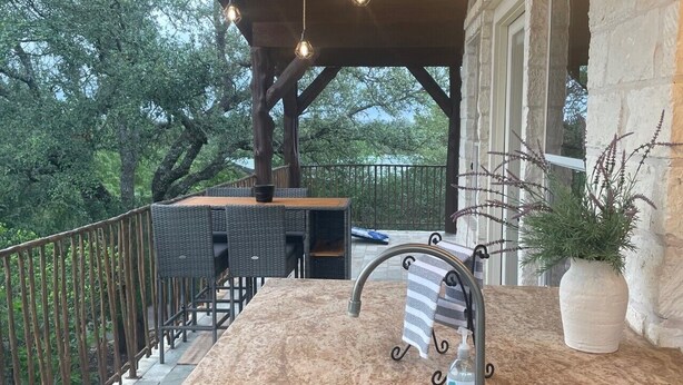An outdoor kitchen with a sink, a dining area with chairs, and string lights. - The Upper Room | 360° Patio Views & Elevated Hill Country Escape (Buda)