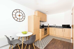 Eine moderne Küche mit Holzschränken, einer schwarzen Mikrowelle und einem runden Tisch mit zwei Stühlen.
