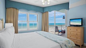 Habitación de hotel con cama, televisor, cómoda y balcón con vista al océano.