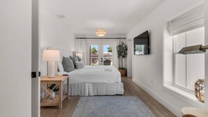 Un dormitorio con cama, mesita de noche, lámpara y vistas al exterior.