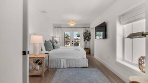 A bedroom with a bed, bedside table, lamp, and a view through a window. - A Salty Cru (Panama City Beach)