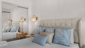 A bedroom with a large bed, bedside lamps, a nightstand, and a mirror. - A Salty Cru (Panama City Beach)