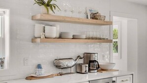 Una cocina con azulejos blancos tipo metro, estantes de madera, una cafetera, un tostador y una figurita decorativa de ballena.