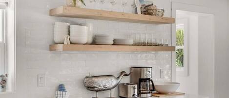 A kitchen with white subway tiles, wooden shelves, a coffee maker, a toaster, and a decorative whale figurine.