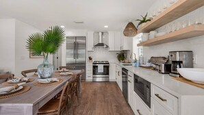 Una cocina moderna con armarios blancos, electrodomésticos de acero inoxidable y un comedor con mesa y sillas de madera.