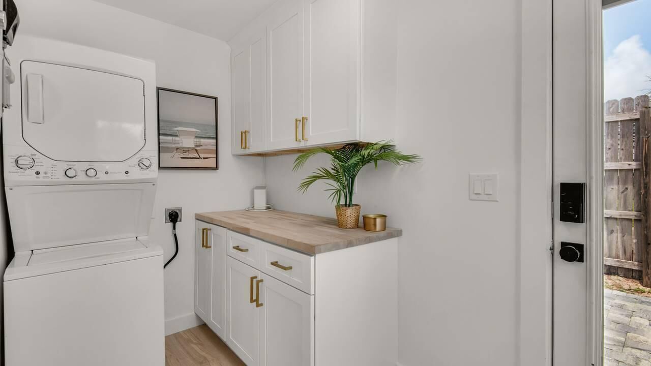 A compact kitchen with white cabinets, a wooden countertop, a small plant, and a framed picture on the wall.