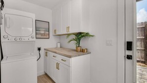 A compact kitchen with white cabinets, a wooden countertop, a small plant, and a framed picture on the wall. - A Salty Cru (Panama City Beach)