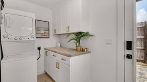 Eine kleine Küche mit weißen Schränken, einer Holz Arbeitsplatte, einem kleinen Topf mit Pflanze und einem gerahmten Bild an der Wand.