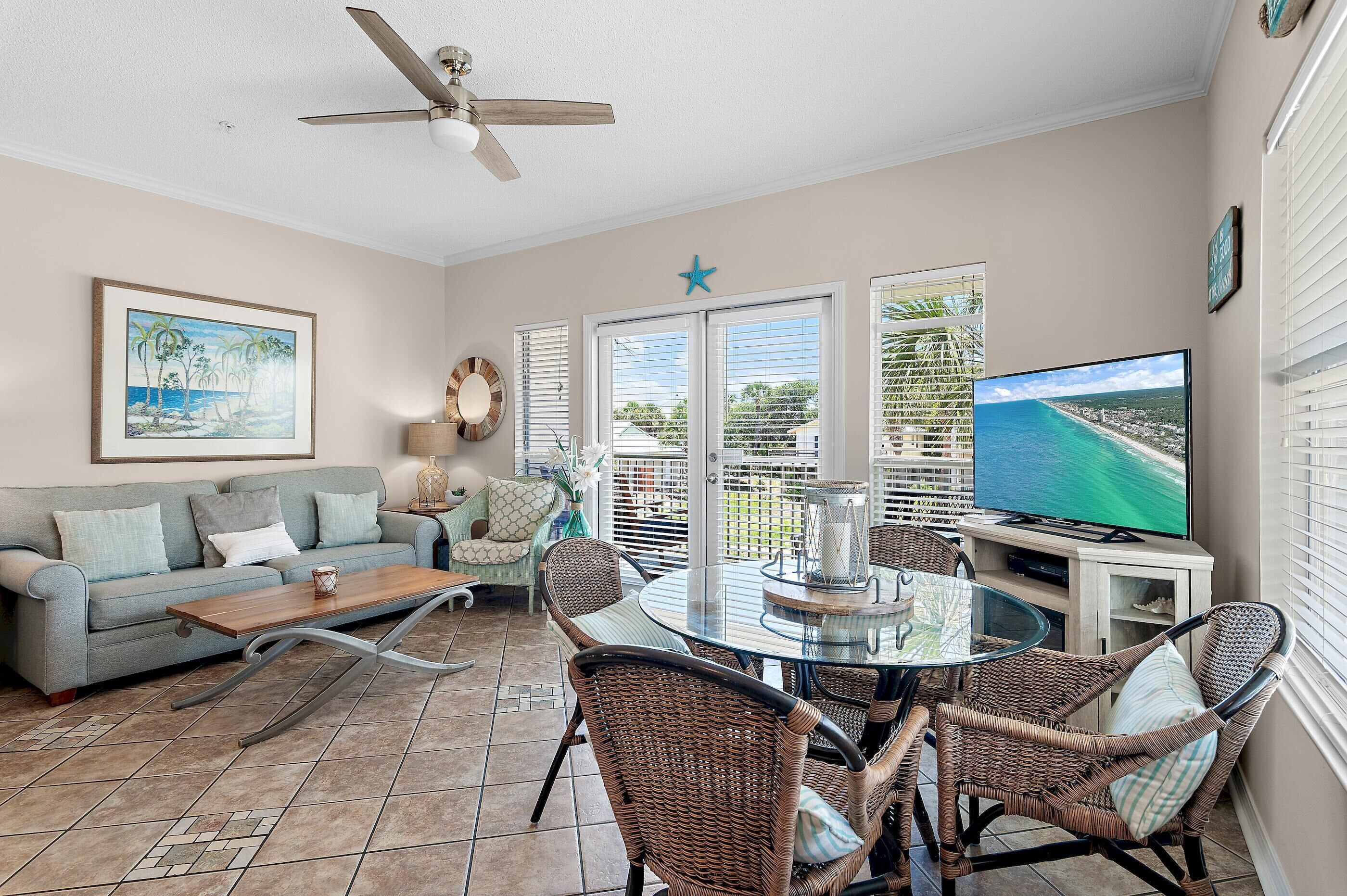 A living room with a sofa, coffee table, wicker chairs, a TV, and a balcony with a view.