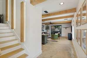 A staircase with wooden steps and a green upholstered chair in a spacious living area with a high ceiling and exposed beams. - Downtown FW Home with City Views, Rooftop, Hot Tub, Walkable to Local Hot Spots (Fort Worth)