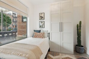 Ein Schlafzimmer mit einem großen Bett, einem Fenster, einem Kleiderschrank und einer Sukkulente.