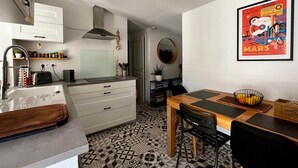 A modern kitchen with a built-in oven, a dining area with a wooden table and chairs, and a colorful Mars-themed artwork on the wall. - BEL AIR - 3-bedroom house with a garden (Mimizan)