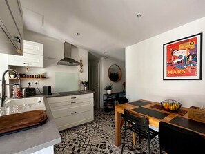 Eine moderne Küche mit Einbauofen, eine Essecke mit Holztisch und -stühlen sowie ein farbenfrohes Kunstwerk mit dem Mars-Motiv an der Wand.