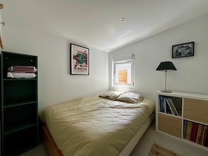 Ein Schlafzimmer mit Bett, Fenster, Bücherregal und Schreibtisch mit Lampe.